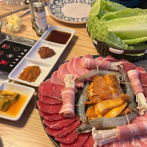 Korean barbecue platter with assorted meats, lettuce, and side dishes on a restaurant table.